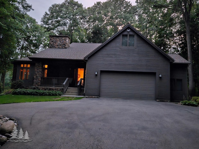 view of front of home featuring a shingled roof, aphalt driveway, covered porch, a chimney, and a garage