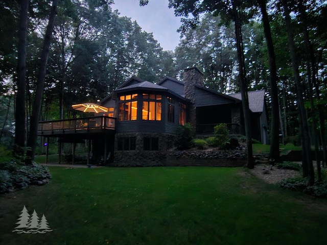 back of property with a chimney, a lawn, stone siding, and a wooden deck