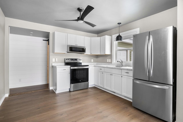 kitchen with a sink, stainless steel appliances, wood finished floors, and white cabinetry