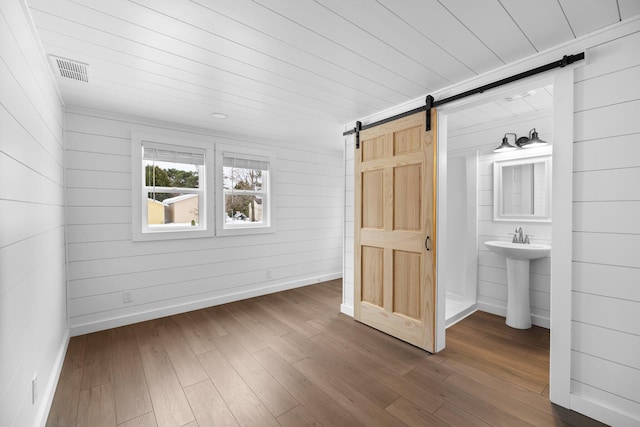 unfurnished bedroom featuring visible vents, baseboards, a barn door, and wood finished floors