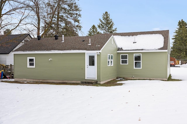 snow covered rear of property with a shingled roof