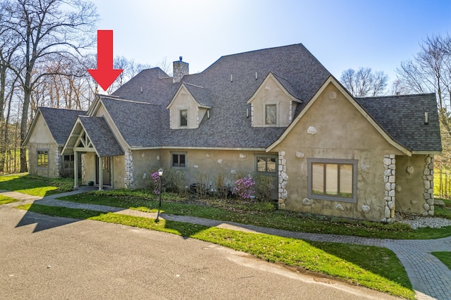 view of front of property with stucco siding, stone siding, roof with shingles, and a chimney