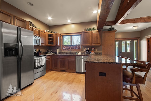 kitchen featuring brown cabinetry, a peninsula, a sink, appliances with stainless steel finishes, and a kitchen bar