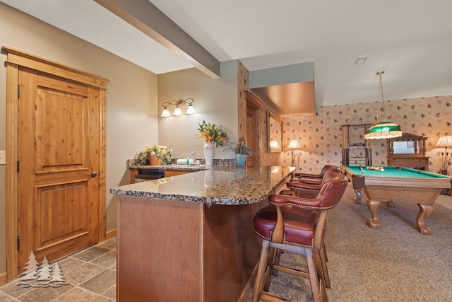 kitchen with beamed ceiling, dark stone counters, a peninsula, pool table, and wallpapered walls