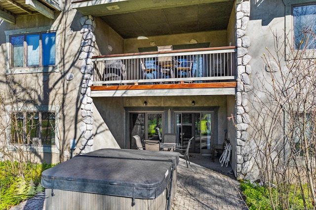 rear view of house featuring a patio area, stucco siding, a hot tub, and a balcony