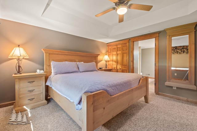 bedroom with ceiling fan, a tray ceiling, baseboards, and light carpet