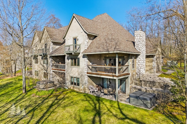 back of house featuring stucco siding, a chimney, a balcony, a yard, and a patio