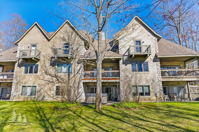 back of property featuring stucco siding, a lawn, and a shingled roof