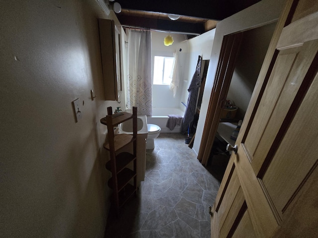 corridor featuring beamed ceiling and stone finish flooring