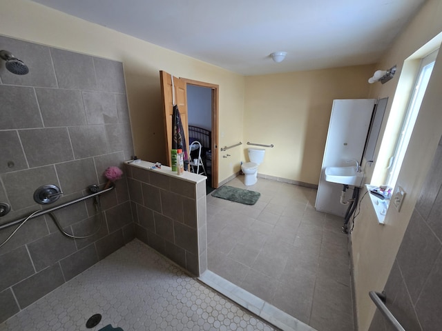 bathroom with baseboards, toilet, a tile shower, tile patterned floors, and a sink