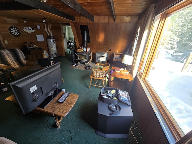 carpeted living room with wooden walls, beamed ceiling, water heater, and a wood stove