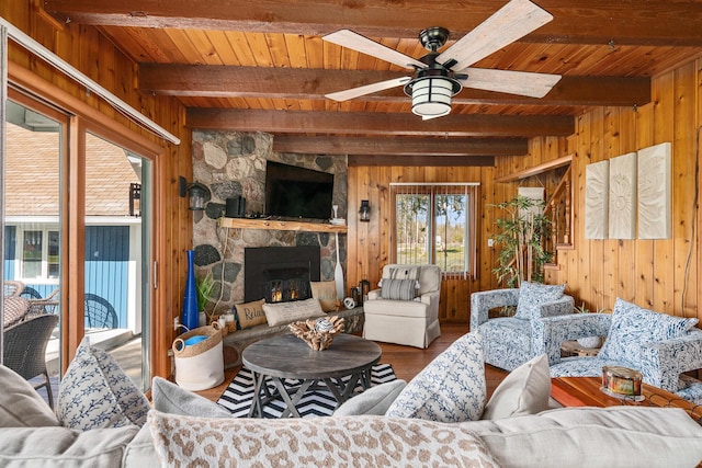 living area featuring wood ceiling, wood finished floors, wood walls, a stone fireplace, and ceiling fan