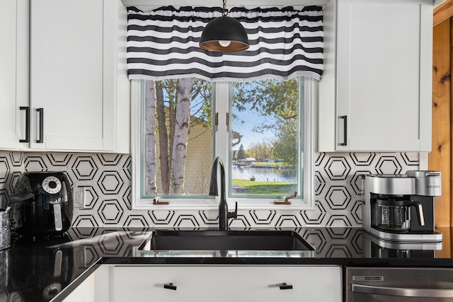 kitchen with white cabinetry, dark countertops, stainless steel dishwasher, and tasteful backsplash