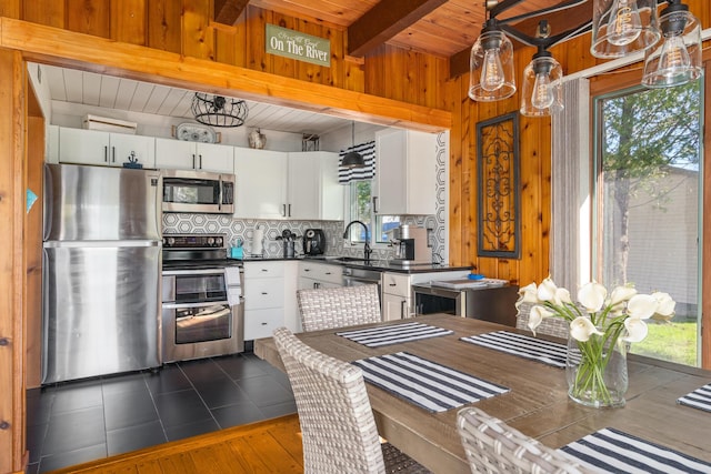 kitchen with tasteful backsplash, wood walls, dark countertops, white cabinets, and appliances with stainless steel finishes