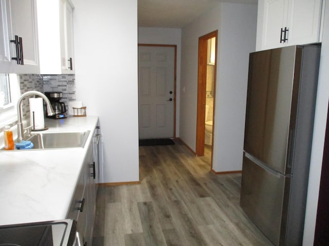 kitchen featuring decorative backsplash, white cabinetry, freestanding refrigerator, and a sink