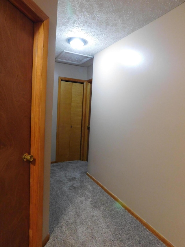 hall with baseboards, a textured ceiling, attic access, and carpet