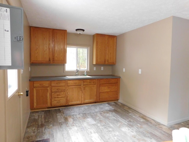 kitchen featuring light wood finished floors, brown cabinetry, baseboards, and a sink