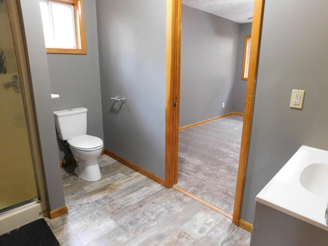 bathroom with toilet, a stall shower, wood finished floors, baseboards, and vanity