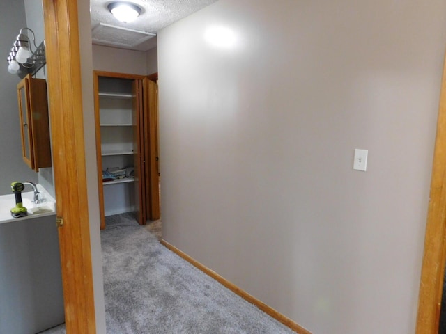 corridor featuring light carpet, attic access, a textured ceiling, and baseboards