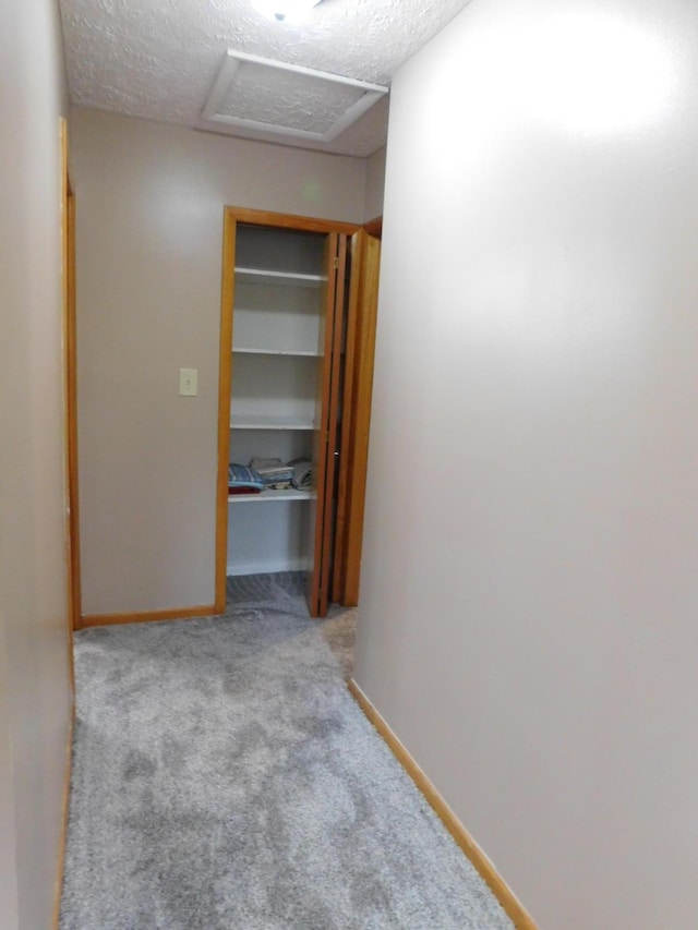 corridor with baseboards, carpet floors, a textured ceiling, and attic access