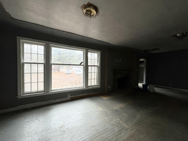 unfurnished living room featuring a fireplace with flush hearth, baseboards, and arched walkways