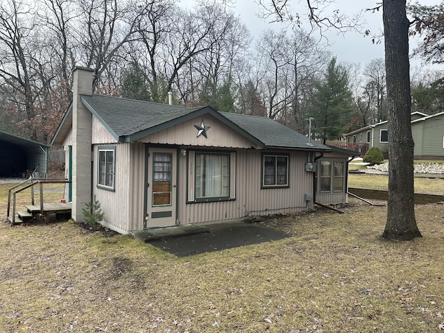 view of front facade with a detached carport, a chimney, and roof with shingles