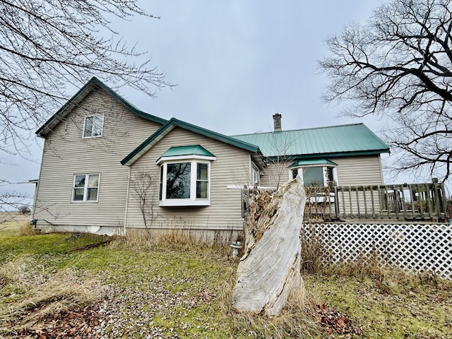 back of house with a deck, a chimney, and metal roof