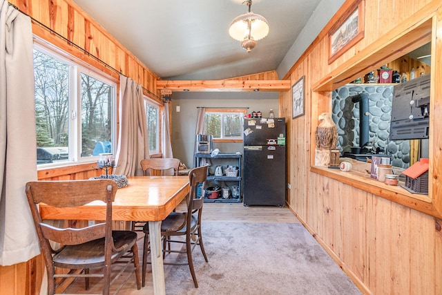 dining space with vaulted ceiling, wooden walls, and light colored carpet