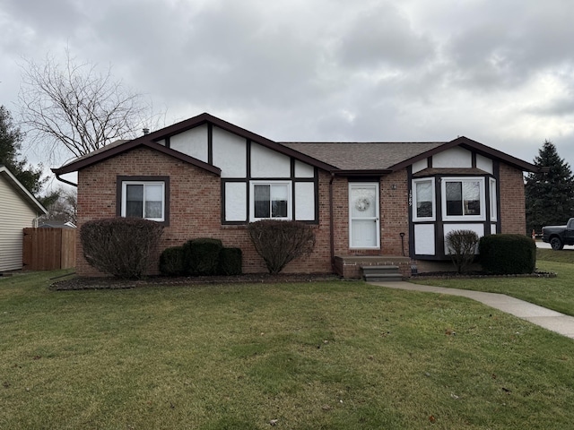 view of front facade with brick siding, roof with shingles, a front lawn, and fence