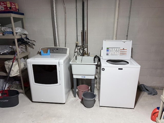 laundry room with washing machine and clothes dryer, concrete block wall, and a sink