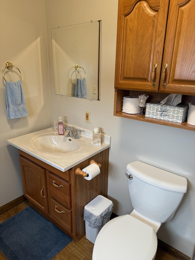 bathroom with toilet, vanity, baseboards, and wood finished floors