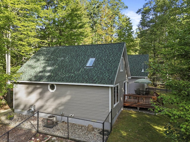 view of home's exterior with a lawn, roof with shingles, a deck, and fence