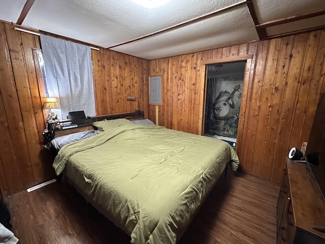 bedroom with dark wood finished floors, wood walls, and a textured ceiling