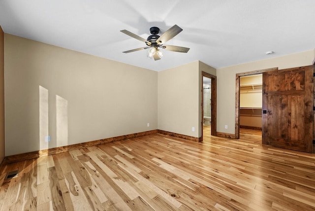 unfurnished bedroom featuring a ceiling fan, baseboards, visible vents, light wood-style flooring, and a spacious closet