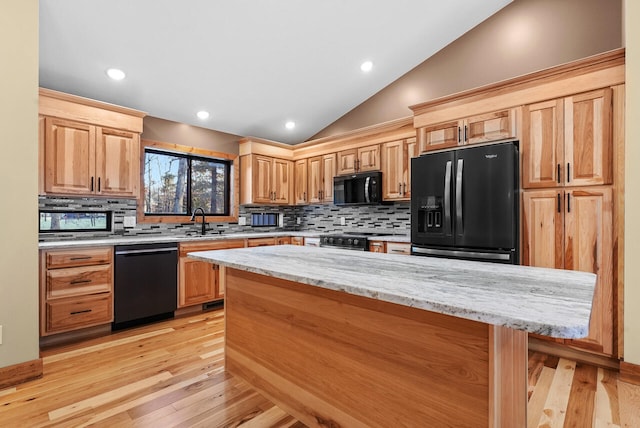 kitchen featuring light stone counters, light wood-style flooring, black appliances, vaulted ceiling, and backsplash