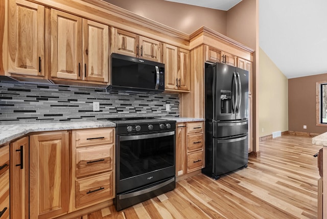 kitchen featuring tasteful backsplash, visible vents, light stone countertops, light wood-style floors, and black appliances