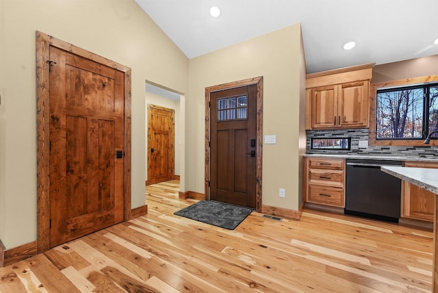 kitchen with backsplash, dishwasher, light countertops, lofted ceiling, and light wood-style flooring