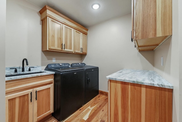 clothes washing area featuring washer and dryer, cabinet space, light wood-style floors, and a sink