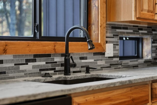 room details with a sink, light stone countertops, backsplash, and dishwasher