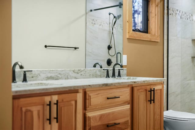 full bath featuring a sink, tiled shower, toilet, and double vanity