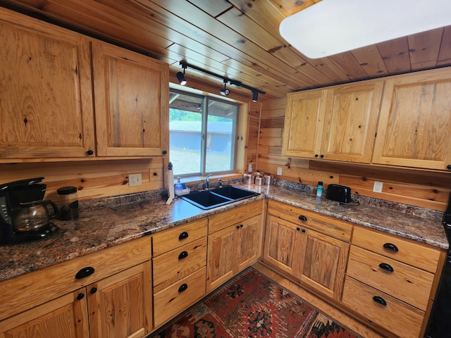 kitchen featuring dark stone countertops, wooden walls, a sink, track lighting, and wood ceiling