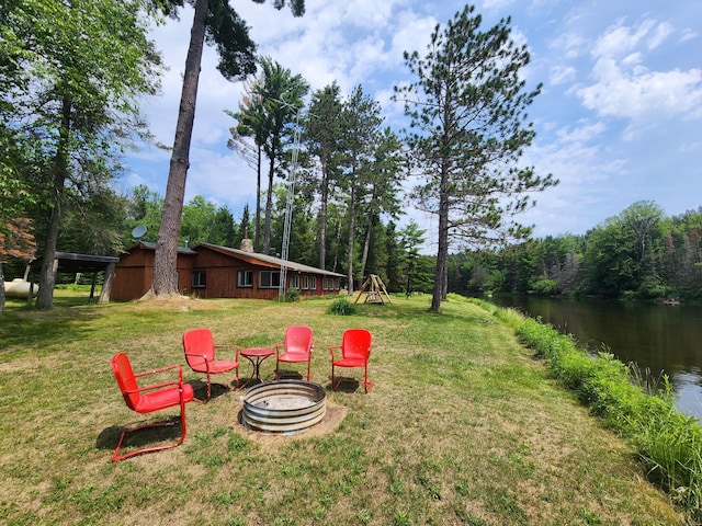 view of yard featuring a fire pit, a forest view, and a water view