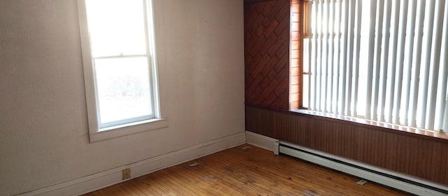 unfurnished room featuring baseboard heating, baseboards, and hardwood / wood-style flooring