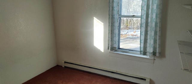 empty room with a textured wall, dark carpet, and a baseboard radiator