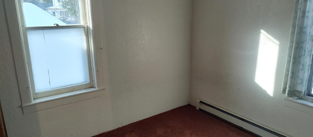 empty room featuring dark carpet, a baseboard heating unit, and a textured wall