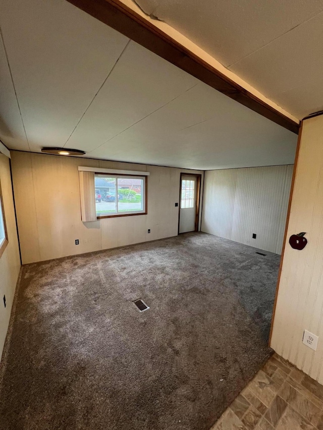 carpeted empty room featuring lofted ceiling with beams and visible vents