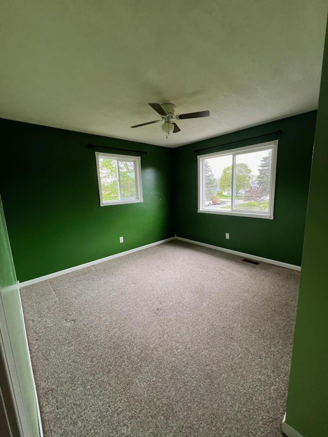 carpeted spare room with a wealth of natural light, visible vents, and baseboards