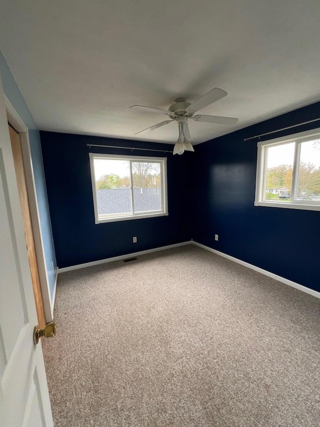 carpeted spare room with visible vents, baseboards, and a ceiling fan