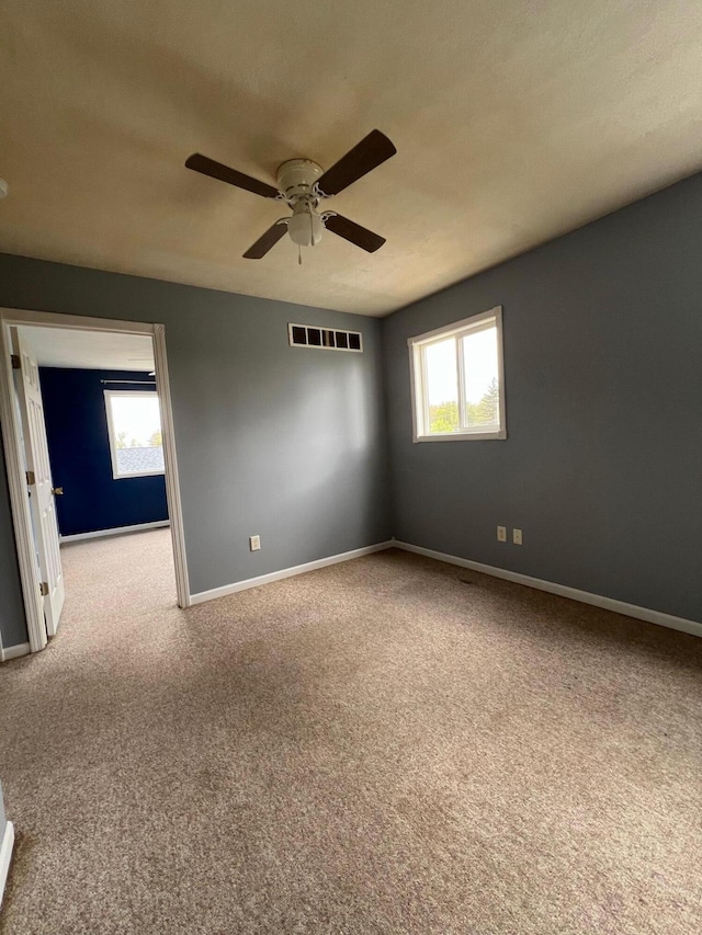 carpeted empty room featuring visible vents, baseboards, a healthy amount of sunlight, and a ceiling fan