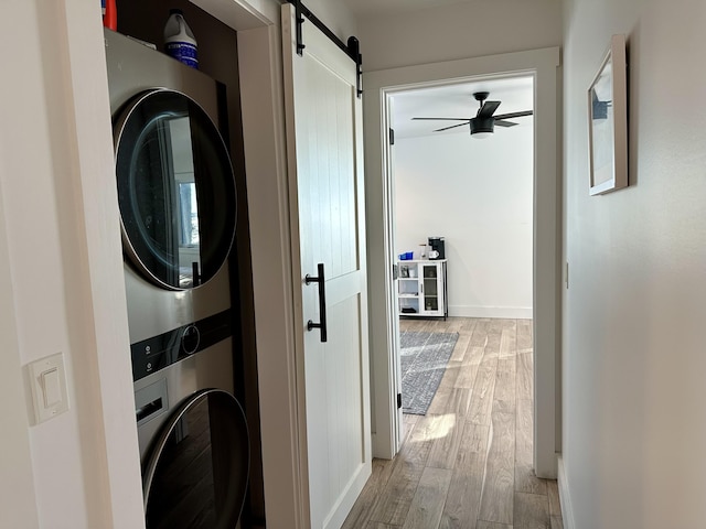 washroom with stacked washer / dryer, ceiling fan, a barn door, laundry area, and light wood-style floors